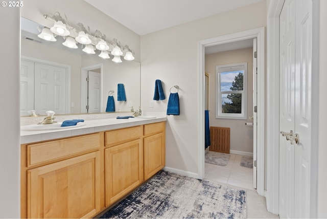 bathroom with a sink, baseboards, tile patterned floors, double vanity, and radiator heating unit