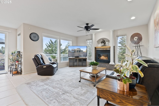 tiled living room featuring a ceiling fan, a glass covered fireplace, a healthy amount of sunlight, and decorative columns