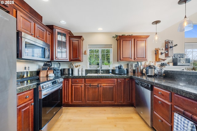 kitchen with appliances with stainless steel finishes, light hardwood / wood-style floors, sink, and hanging light fixtures