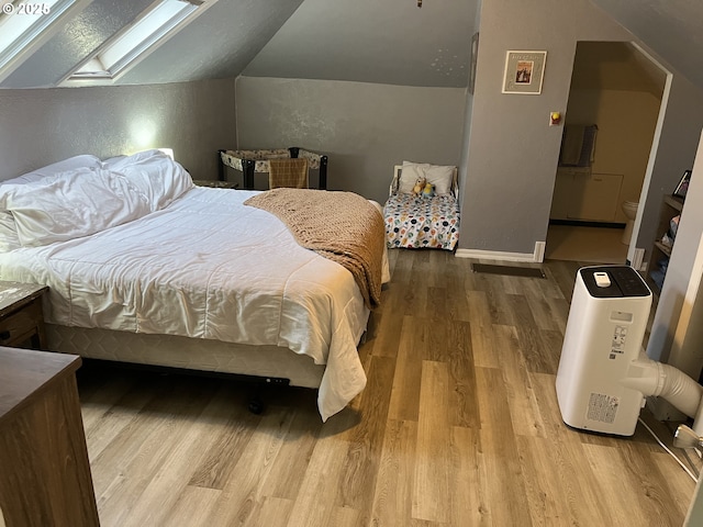 bedroom with vaulted ceiling with skylight and hardwood / wood-style floors