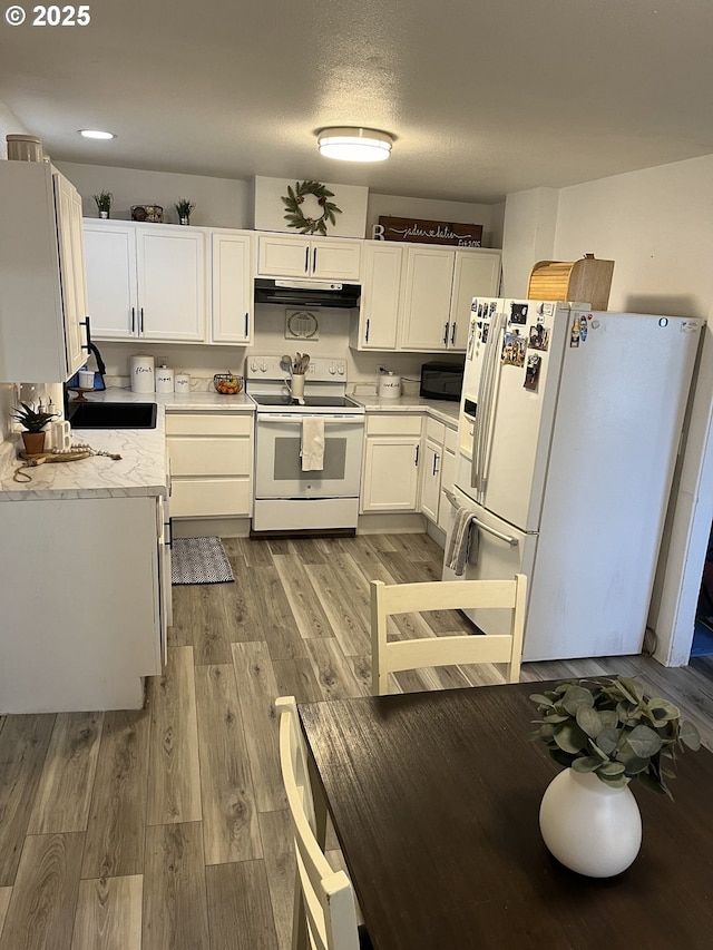 kitchen with white cabinets, white appliances, a textured ceiling, and light hardwood / wood-style flooring