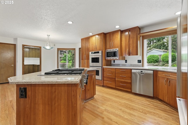 1324 Stonehaven Dr, West Linn, OR 97068 - kitchen with appliances with stainless steel finishes, brown cabinets, a textured ceiling, a center island, and light wood-style floors