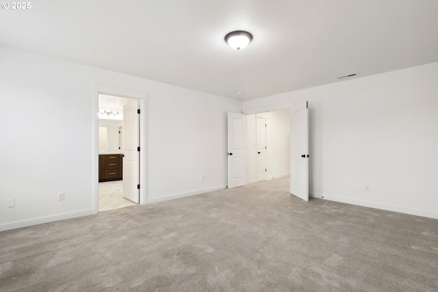 unfurnished bedroom featuring light carpet and ensuite bath