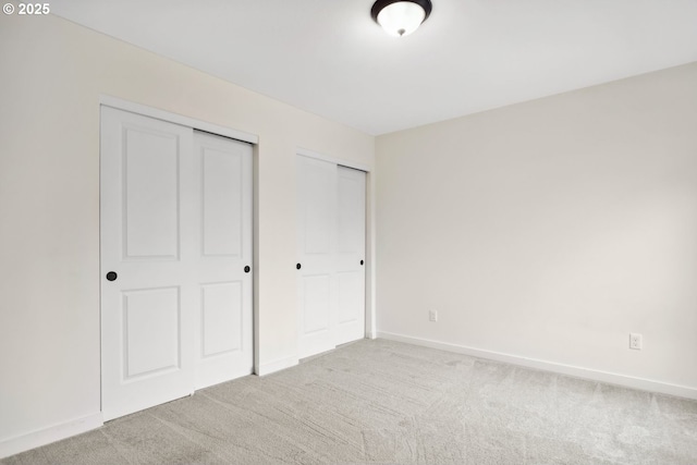 unfurnished bedroom featuring light carpet and multiple closets