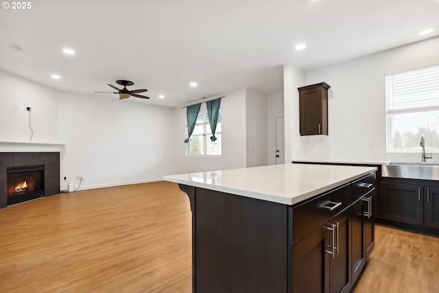 kitchen featuring a center island, sink, light wood-type flooring, a tiled fireplace, and ceiling fan