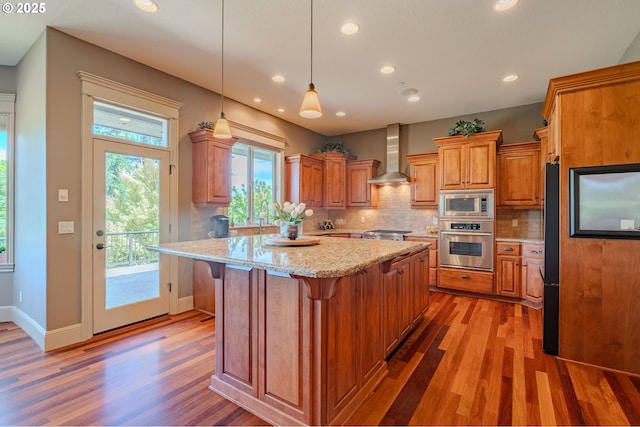 21106 NW 3rd Ct, Ridgefield, WA 98642 - kitchen with stainless steel appliances, wall chimney range hood, light wood-style flooring, decorative backsplash, and a center island