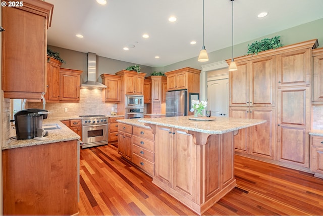 21106 NW 3rd Ct, Ridgefield, WA 98642 - kitchen with wall chimney range hood, appliances with stainless steel finishes, a kitchen island, a breakfast bar area, and light wood-style flooring