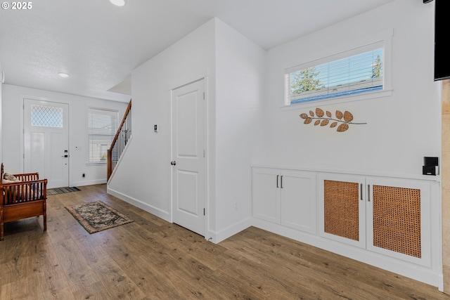 foyer featuring a healthy amount of sunlight, stairway, baseboards, and wood finished floors