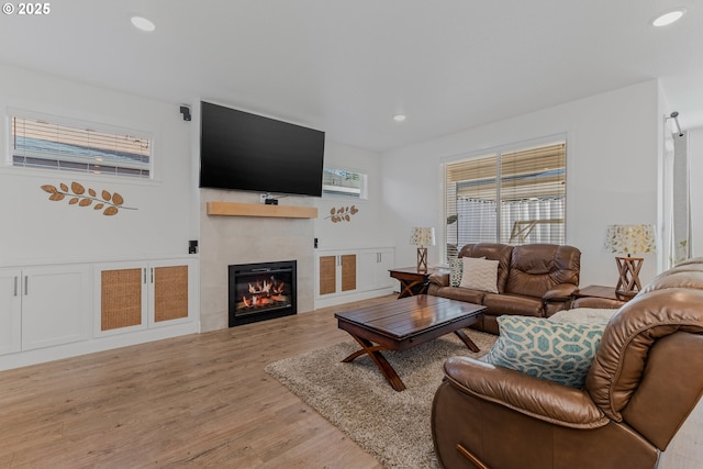 living area with light wood finished floors, a tile fireplace, and recessed lighting