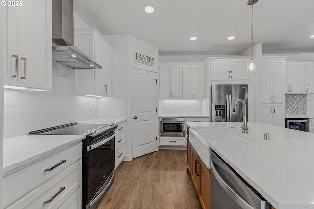 kitchen featuring white cabinets, wall chimney exhaust hood, appliances with stainless steel finishes, decorative light fixtures, and a sink