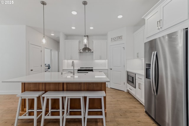 kitchen featuring stainless steel appliances, white cabinetry, light countertops, wall chimney exhaust hood, and a center island with sink