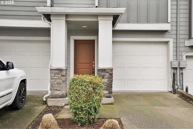 doorway to property featuring board and batten siding, stone siding, driveway, and a garage