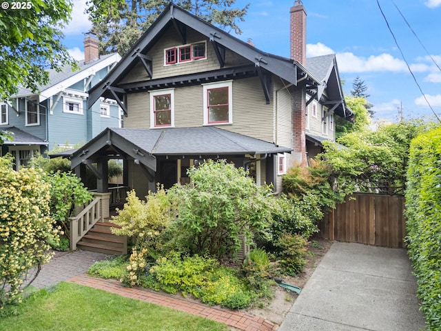 victorian-style house with covered porch, fence, roof with shingles, and a chimney