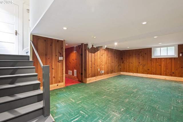 below grade area with visible vents, baseboards, stairway, wooden walls, and recessed lighting