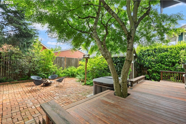 wooden terrace with a fenced backyard, a patio area, a fire pit, and a hot tub