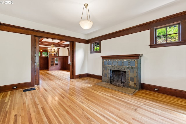 unfurnished living room featuring an inviting chandelier, light wood-type flooring, a tiled fireplace, and baseboards