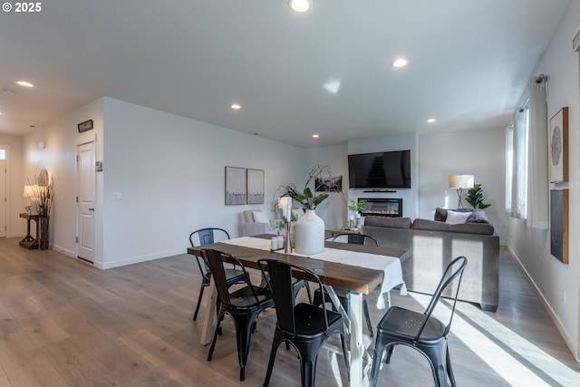 dining space with light wood-style floors, recessed lighting, baseboards, and a glass covered fireplace