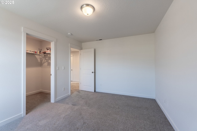 unfurnished bedroom featuring carpet, a walk in closet, visible vents, a textured ceiling, and baseboards