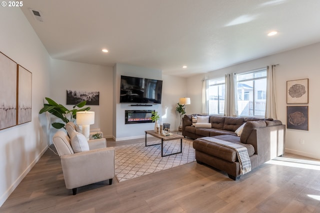 living area featuring a glass covered fireplace, wood finished floors, visible vents, and recessed lighting