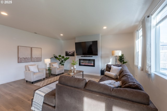 living room featuring a glass covered fireplace, plenty of natural light, wood finished floors, and recessed lighting