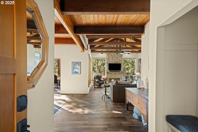 interior space featuring dark wood-type flooring, a ceiling fan, a stone fireplace, wooden ceiling, and beamed ceiling