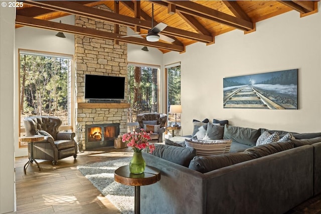 living area featuring lofted ceiling with beams, wood finished floors, a wealth of natural light, and a stone fireplace