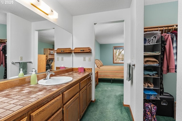 bathroom with vanity, a walk in closet, baseboards, and a textured ceiling