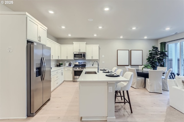 kitchen with light countertops, a kitchen bar, appliances with stainless steel finishes, light wood-style floors, and a sink