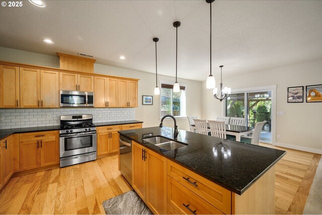 kitchen with light wood-style flooring, appliances with stainless steel finishes, decorative backsplash, and a sink