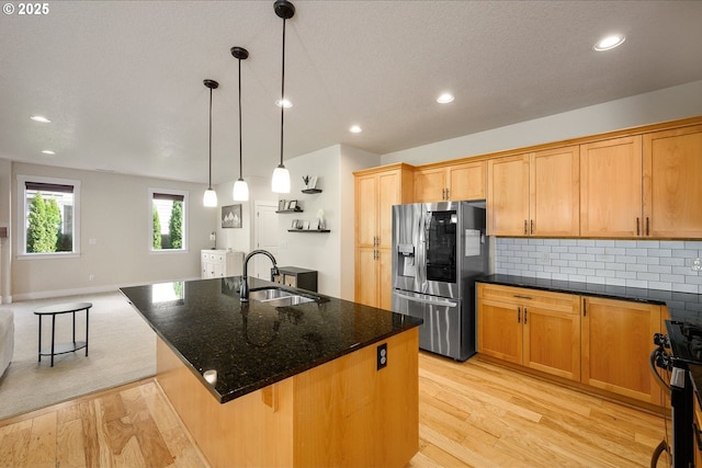 kitchen with backsplash, appliances with stainless steel finishes, light wood-style floors, a sink, and dark stone countertops