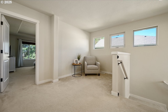 living area featuring baseboards, light carpet, a textured ceiling, and an upstairs landing