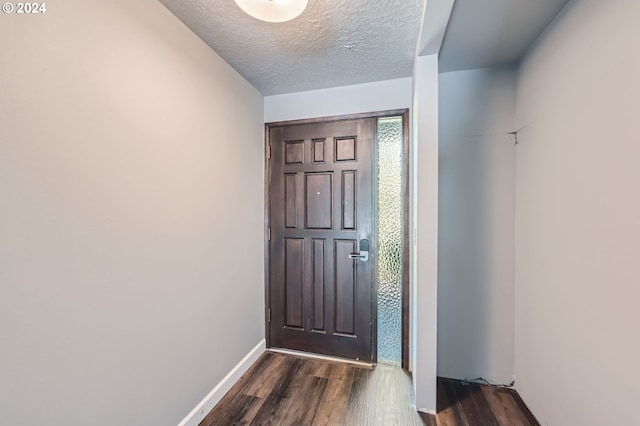 doorway with baseboards, a textured ceiling, and dark wood-style flooring
