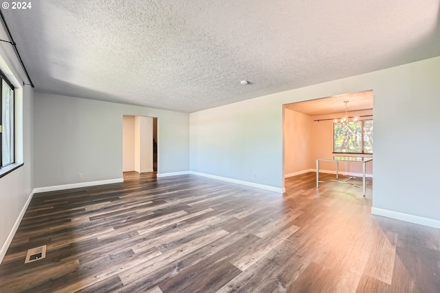 spare room featuring a textured ceiling, baseboards, a chandelier, and dark wood finished floors