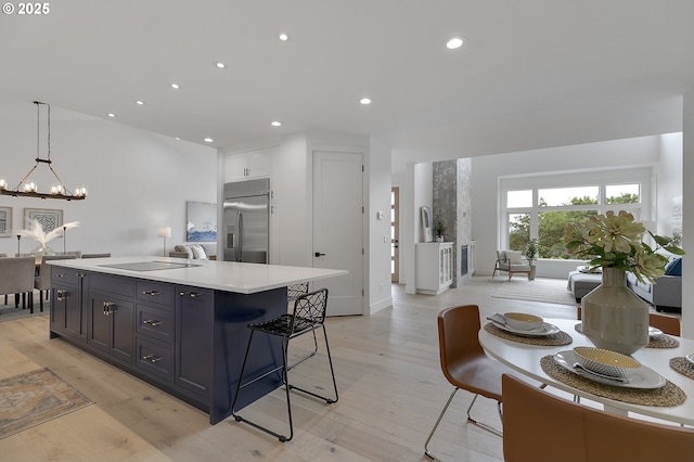 kitchen with white cabinetry, decorative light fixtures, built in fridge, a notable chandelier, and a kitchen island with sink