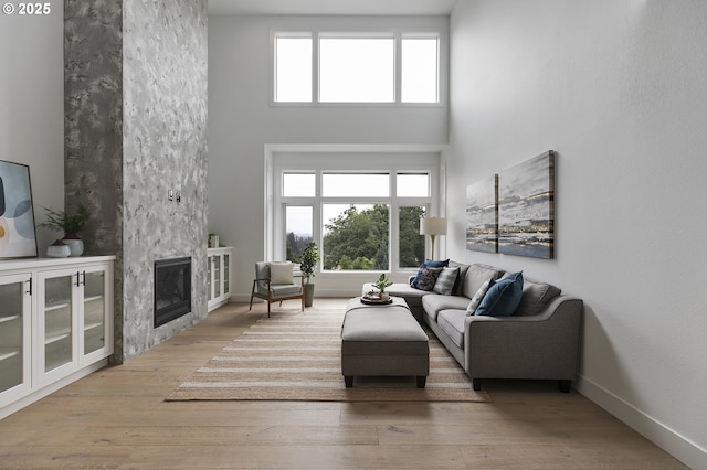 living room featuring plenty of natural light, a fireplace, a high ceiling, and light wood-type flooring