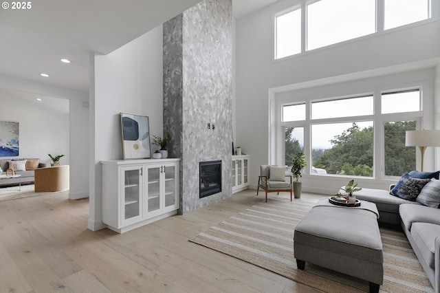 living room with a towering ceiling, a high end fireplace, and light wood-type flooring