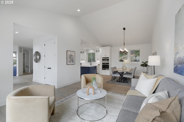 living room featuring plenty of natural light, a notable chandelier, high vaulted ceiling, and light hardwood / wood-style flooring