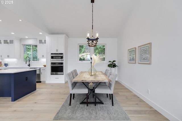 dining space featuring vaulted ceiling, sink, a chandelier, and light hardwood / wood-style floors