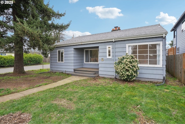 back of house with a lawn, roof with shingles, and fence