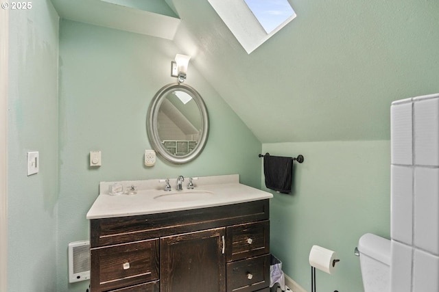 bathroom with toilet, vanity, and lofted ceiling with skylight