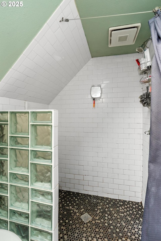 bathroom with a tile shower and lofted ceiling