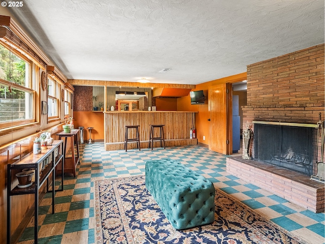 living area featuring a brick fireplace, wood walls, and a textured ceiling