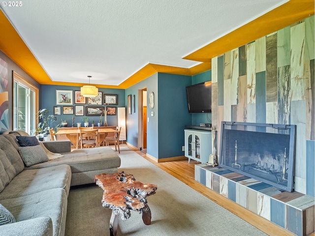 living room featuring baseboards, a textured ceiling, a raised ceiling, and wood finished floors