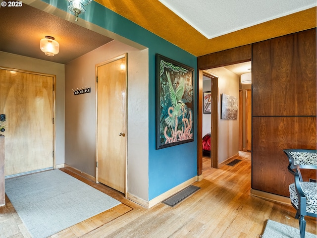 hallway with visible vents, a textured ceiling, baseboards, and wood finished floors