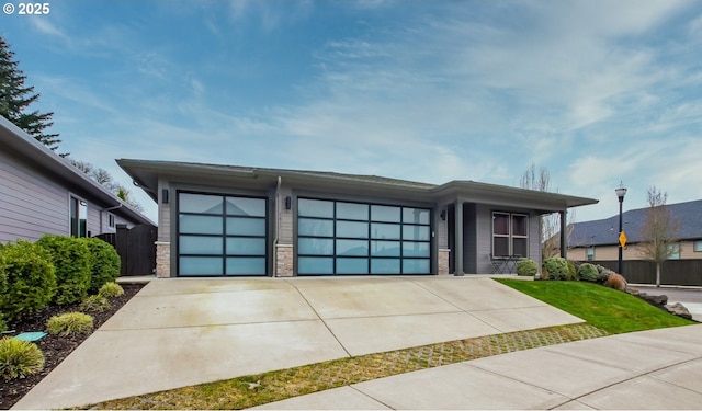 view of front of house featuring stone siding, driveway, a garage, and fence