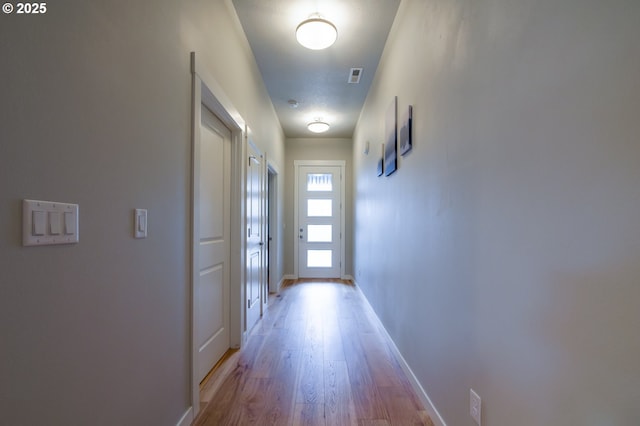 hallway featuring visible vents, light wood-type flooring, and baseboards