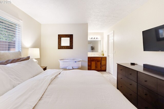 bedroom with connected bathroom, a textured ceiling, and light colored carpet