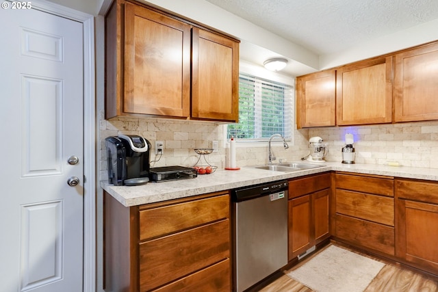 kitchen featuring stainless steel dishwasher, a sink, backsplash, light countertops, and a textured ceiling