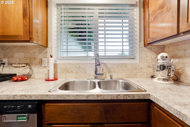 kitchen featuring a sink, dishwasher, backsplash, light countertops, and brown cabinetry