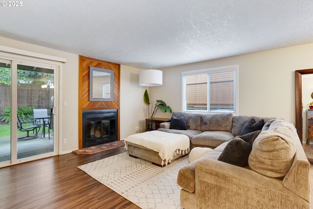 living room with wood finished floors, healthy amount of natural light, a textured ceiling, a large fireplace, and baseboards